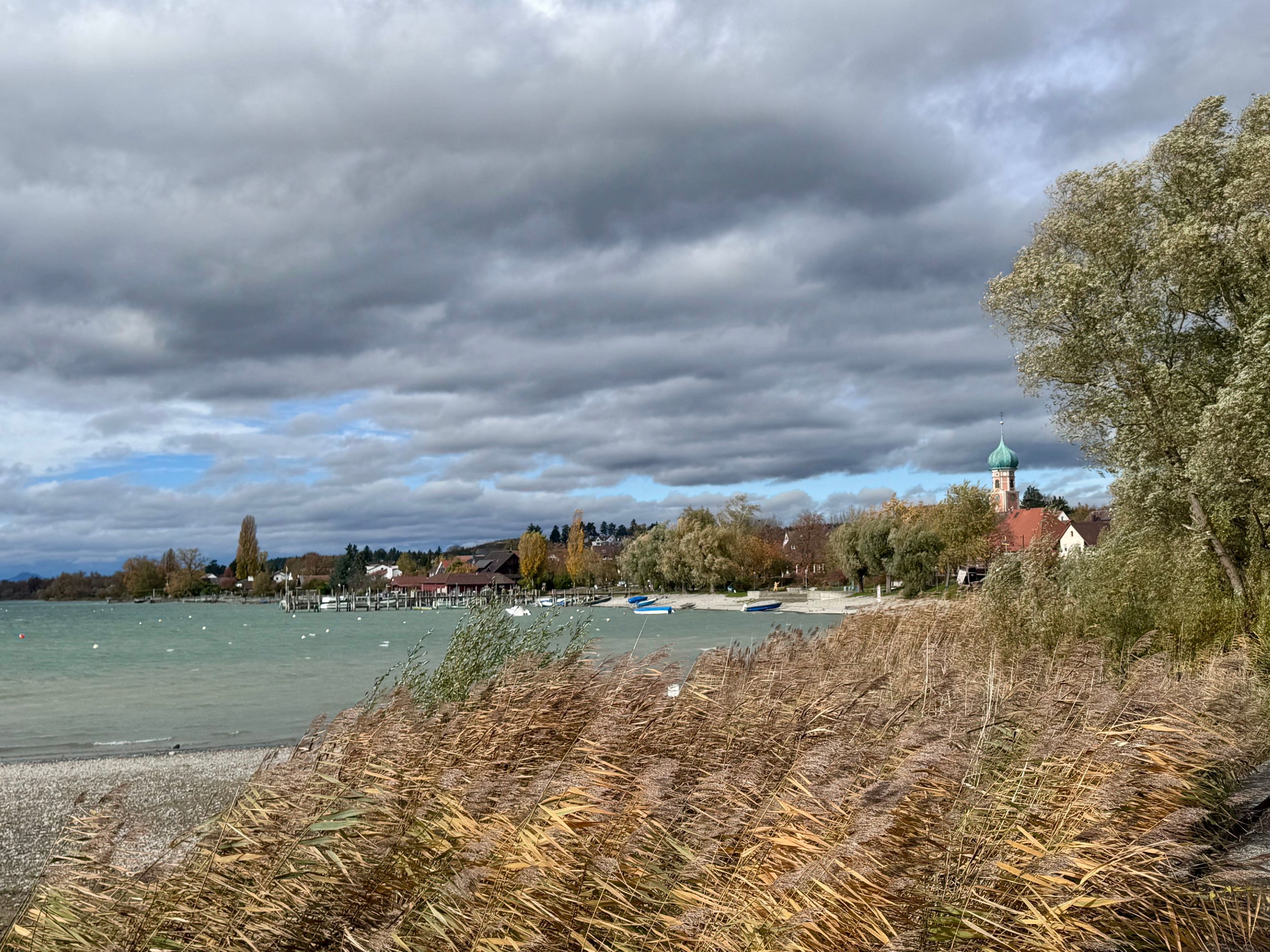 Vista de un lago con barcos, una iglesia con cúpula verde y una zona boscosa.