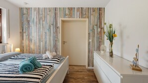 A bedroom with a bed, a dresser, a door, and a wall with vertical wooden planks.