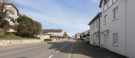 Une rue résidentielle tranquille, bordée de maisons, avec un ciel dégagé et un mur de pierre sur le côté gauche.