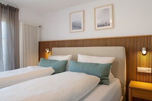 Une chambre d’hôtel avec deux lits, une tête de lit en bois, des lampes fixées au mur et deux tableaux encadrés.