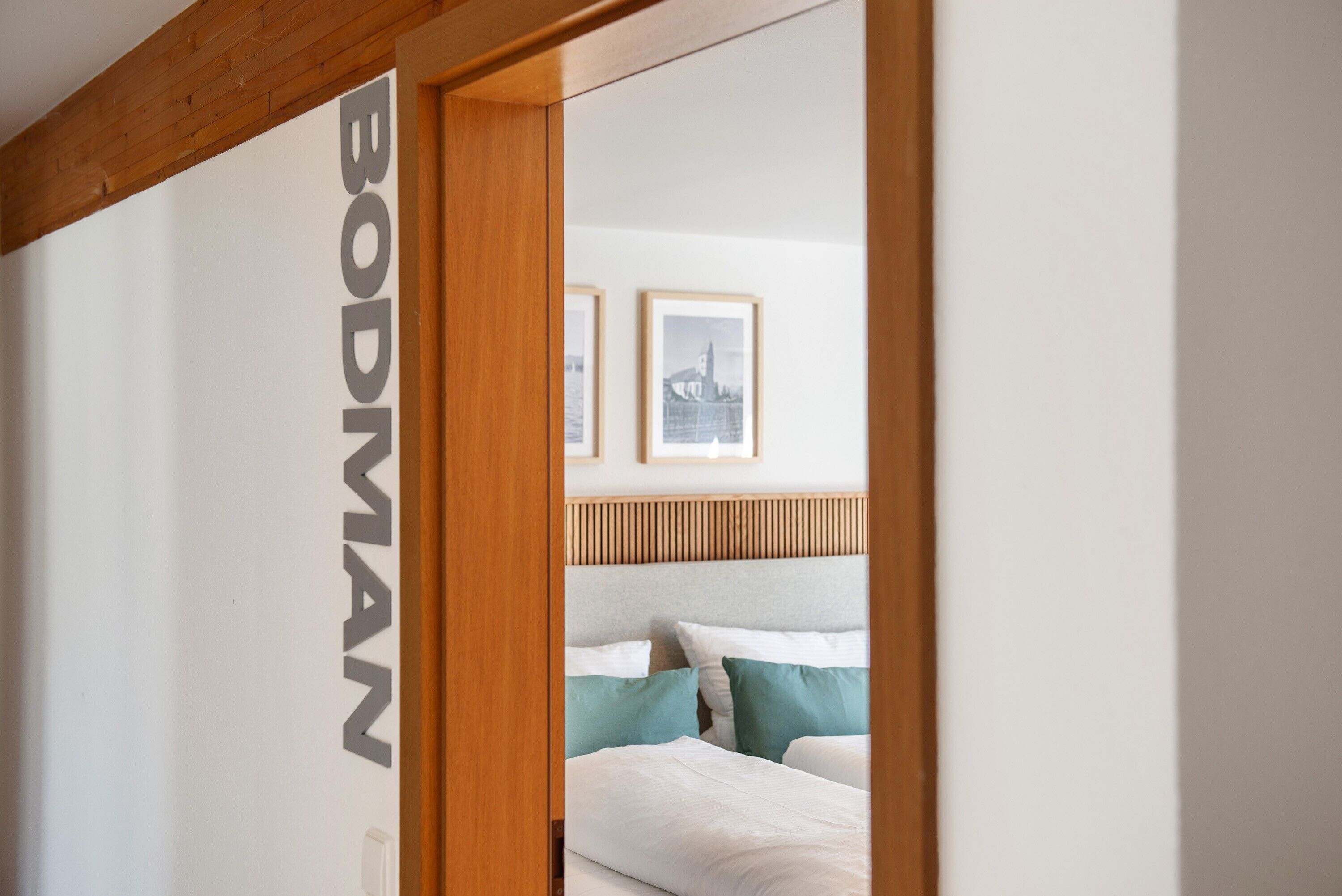 A bedroom with a bed, pillows, a headboard, and a wall with the word 'BODMAN' visible.