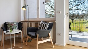 Une pièce avec une fenêtre, un radiateur, une chaise, une table et une lampe.