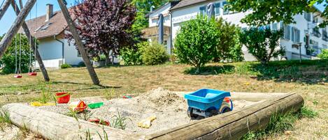 A wooden play area with sand, a blue toy truck, and various toys.