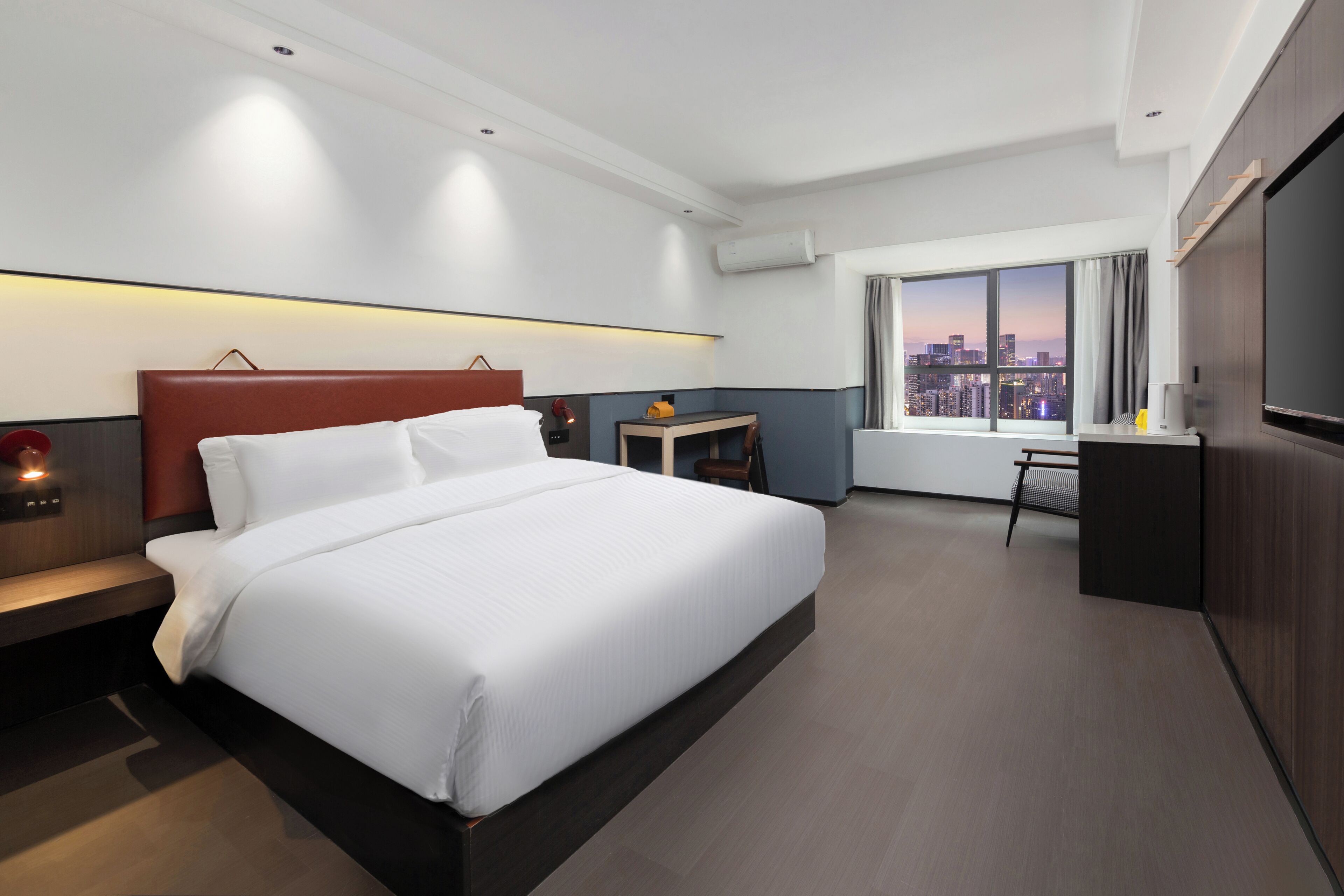 A modern hotel room with a large bed, bedside tables, a desk, and a city view.