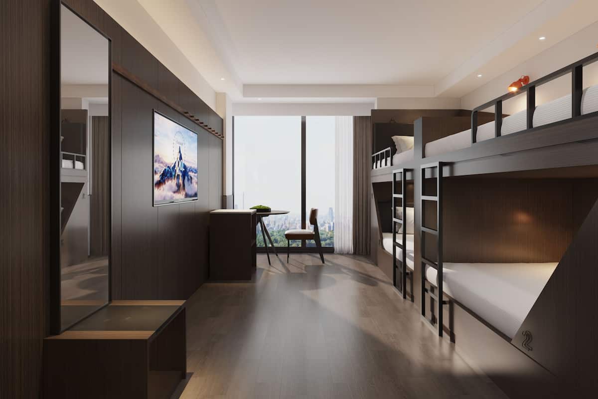 A modern hotel room with a large TV, a bunk bed, a desk, and a view of the city.