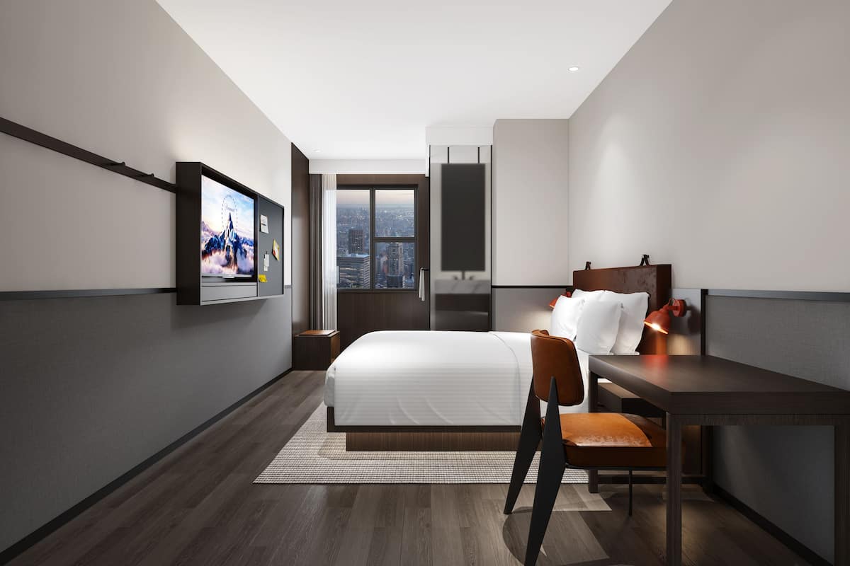 A modern hotel room with a large bed, a desk, a chair, and a TV mounted on the wall.