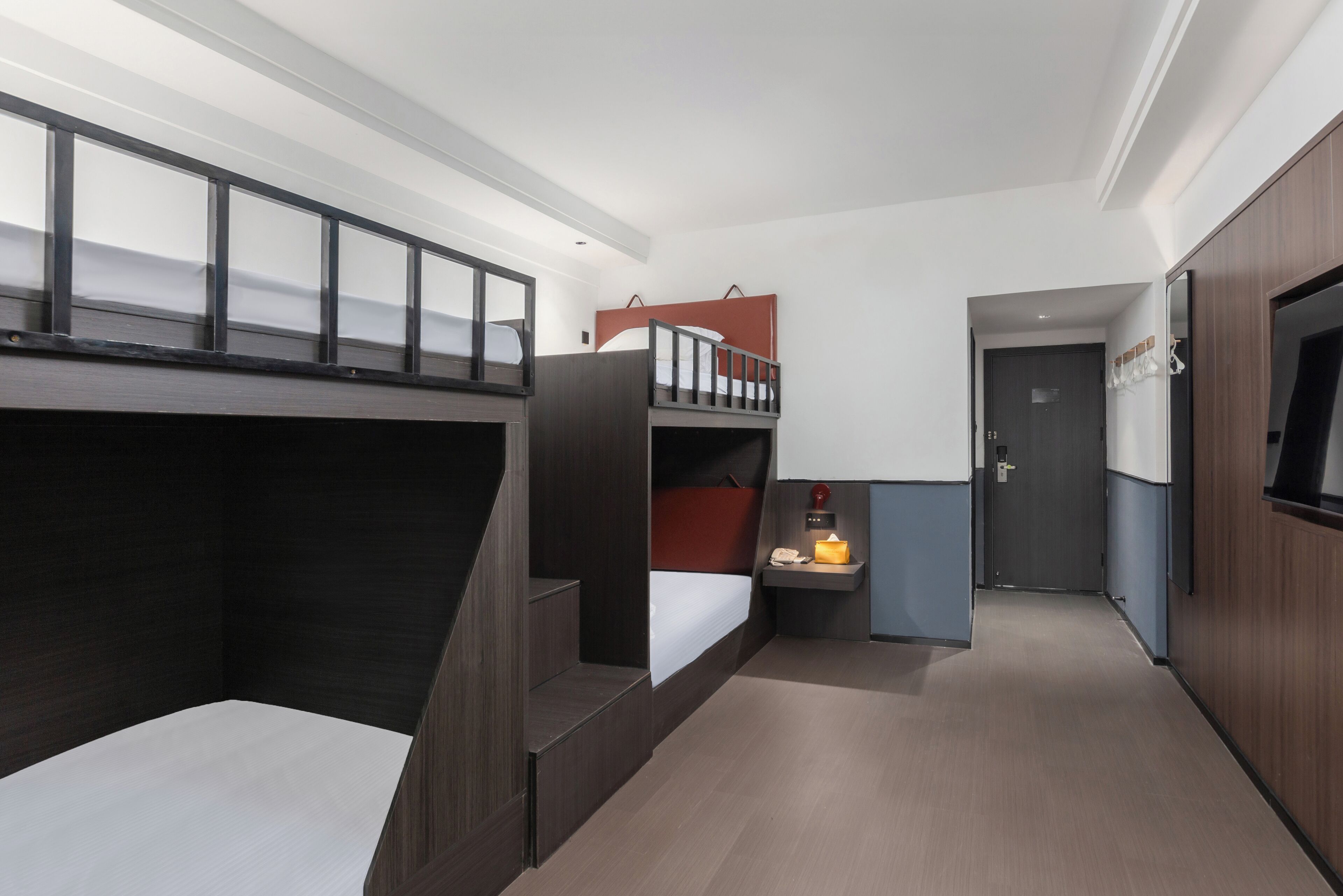A modern hotel room with bunk beds, a small desk with a lamp, and a wardrobe.