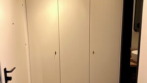 Huoneessa on puulattia, penkki ja valkoinen vaatekaappi, jossa on peili.