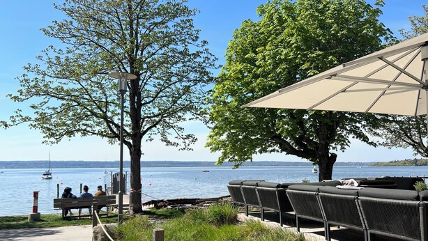 Järvenrantainen oleskelualue, josta avautuu näkymä vedelle, puulle ja penkille.