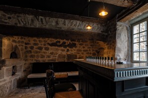 A stone-walled room with a bar area, a bench, and a window.