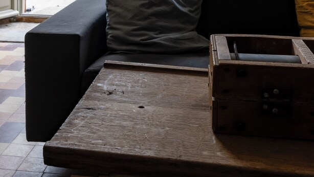 Une pièce avec un canapé noir, une table en bois et une vue sur une piscine, visible à travers une porte ouverte.