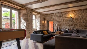 Une pièce aux murs de pierre, avec des poutres apparentes, une table de billard, un canapé et un sol à motifs.