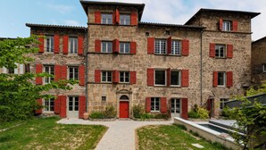 Un bâtiment en pierre avec des volets rouges, une entrée centrale et un chemin pavé menant à la porte.