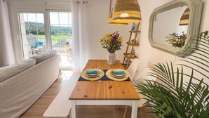 Un comedor con una mesa de madera, sillas blancas, un banco y una lámpara de mimbre colgante.