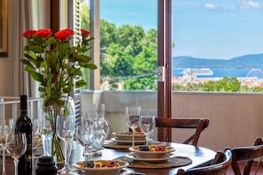 A dining table set with wine glasses, plates, and a vase of red roses, overlooking a scenic view of a coastal town. - Sardinia Re - Villino Silvia (Alghero)