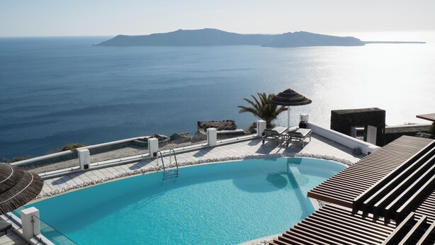 A pool with a view of the sea and a wooden deck with lounge chairs. - Two-Bedroom Caldera View (Thira - Santorini)
