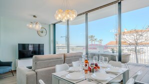 Un salon moderne avec un canapé, un téléviseur et un coin repas équipé d’une table pour quatre personnes.