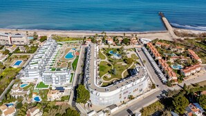 Vue aérienne d’une station balnéaire dotée de plusieurs piscines, d’un port de plaisance et d’une plage.