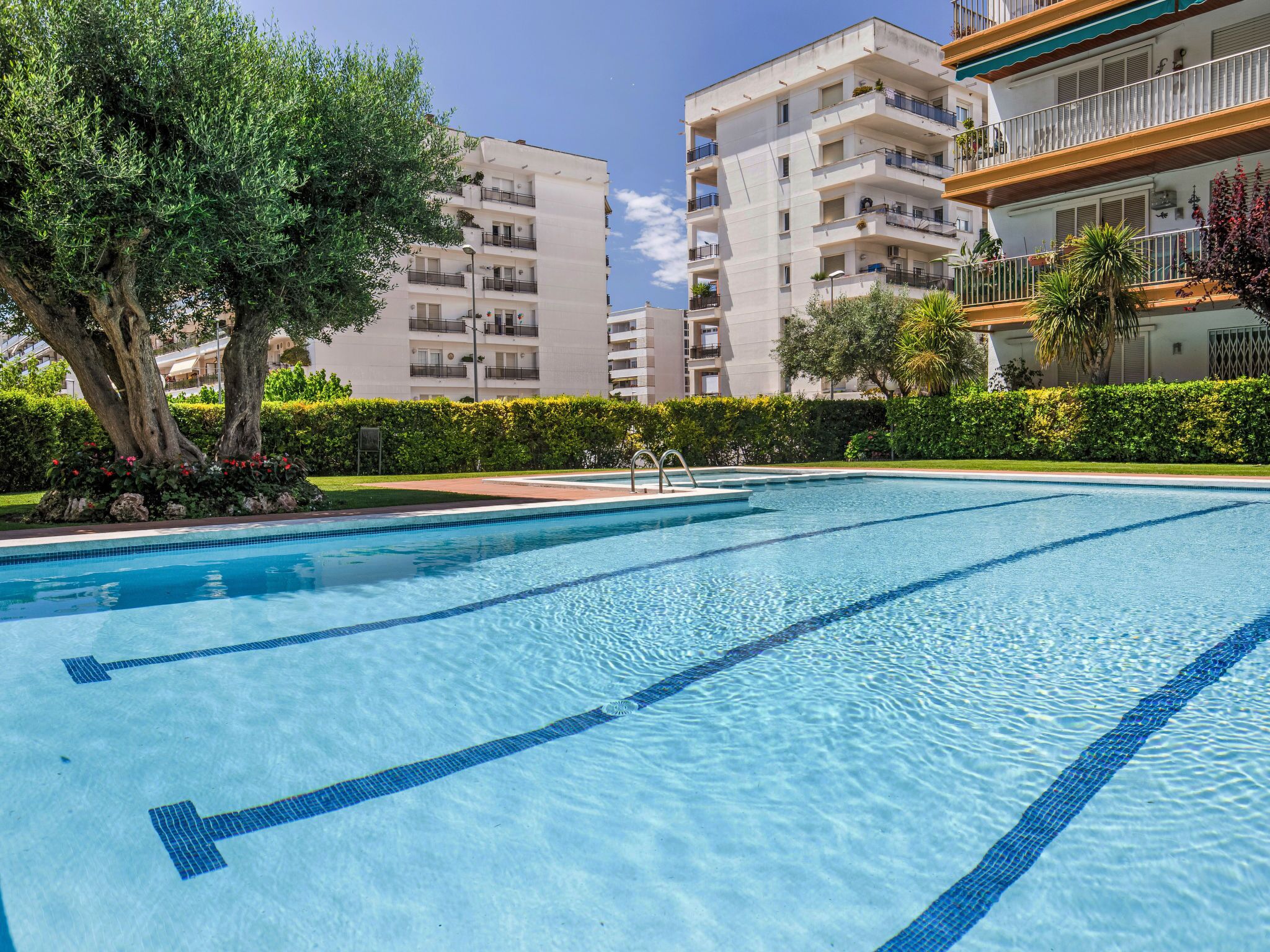 A swimming pool with clear blue water, surrounded by greenery and modern apartment buildings.