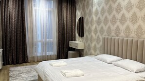 Moderni hotellihuone, jossa on suuri sänky, yöpöytä, peili ja ikkuna, jossa on verhot.