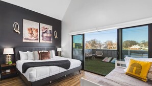 Een moderne slaapkamer met een groot bed, een balkon met buitenmeubels en kunst aan de muur.