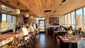 Een restaurant met houten plafond, lange tafels en stoelen, mensen aan het dineren en uitzicht.