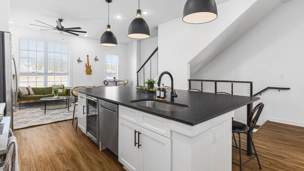 Een moderne keuken met een centraal eiland, zwarte hanglampen en een trap die naar een hoger niveau leidt.