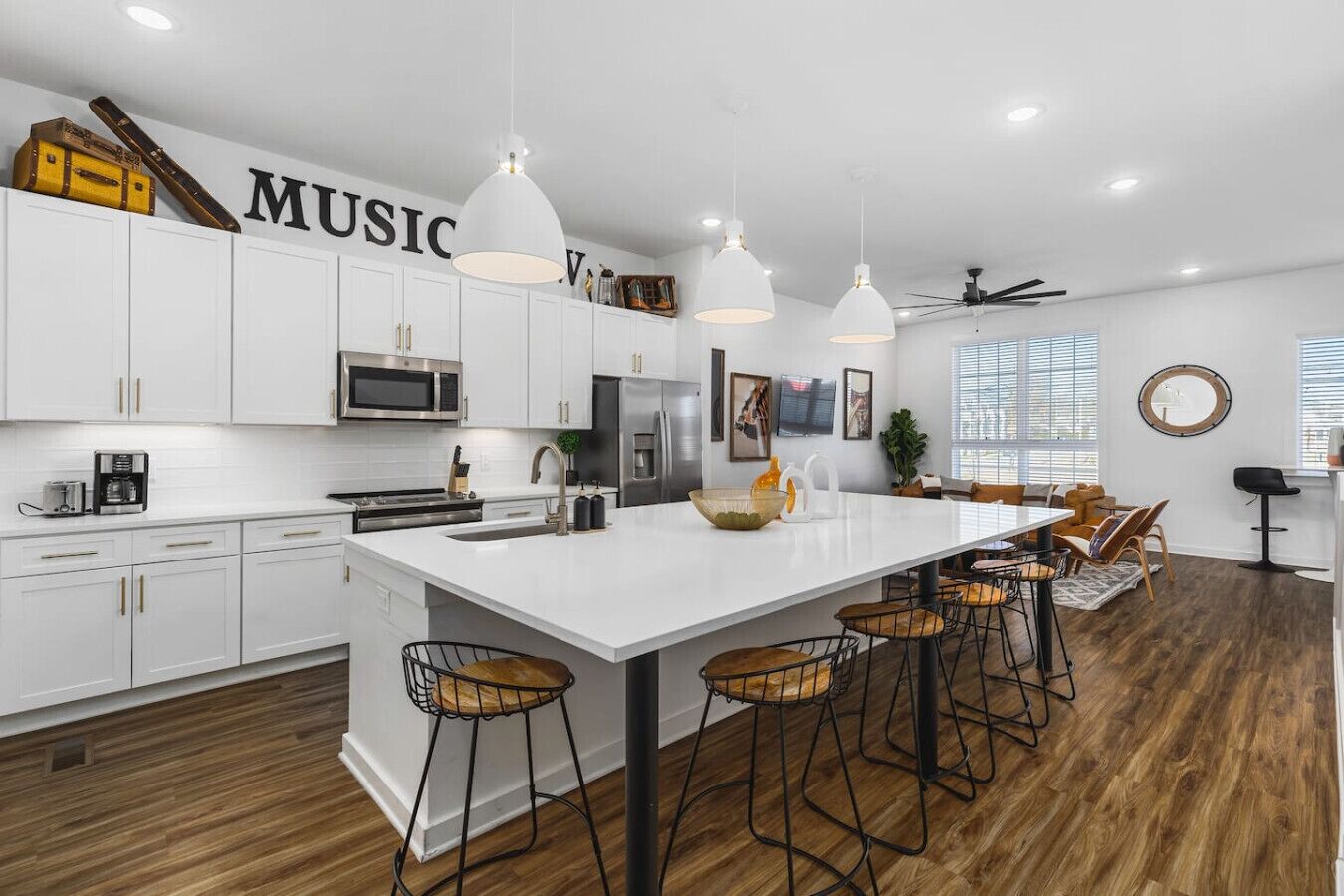 A modern kitchen with white cabinets, a large island with bar stools, and pendant lighting.