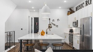 Een moderne keuken met een centraal eiland, barstoelen, een hanglamp en een aan de muur bevestigde gitaar.