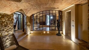 Un pasillo amplio con techo alto y rústico y paredes de piedra. Se ve una gran y ornamentada puerta con una estatua en frente.