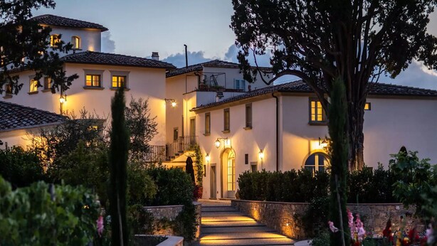 Una villa con un camino de piedra que conduce a la entrada, rodeada de abundante vegetación y plantas en flor.