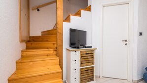 A wooden staircase with a television on a cabinet, a white door, and a small storage unit.