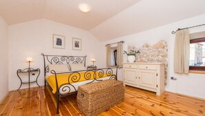 A bedroom with a bed, bedside tables, a dresser, a stone wall, and a window with curtains.
