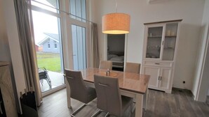 A modern dining area with a glass table, two chairs, a hanging light fixture, and a view of the outdoors.