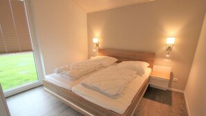 A bedroom with a wooden bed, two bedside lamps, and a view of a grassy area through a window.