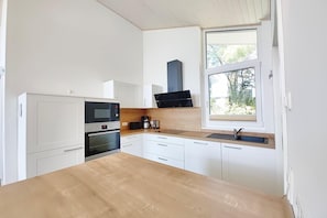 A modern kitchen with white cabinets, a wooden countertop, a built-in oven, a coffee maker, and a window with a view of greenery. - Ferienhaus mit Sauna im Mirow (Granzow)