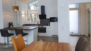 Eine moderne Küche mit weißen Schränken, einer schwarzen Mikrowelle und einem eingebauten Backofen. Es gibt einen Essbereich mit einem Holztisch und zwei Stühlen.