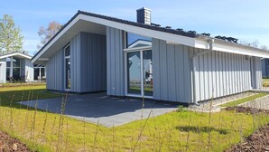 Ein modernes Haus mit großem Glasflurgang, einer überdachten Terrasse und einem gepflegten Rasen.