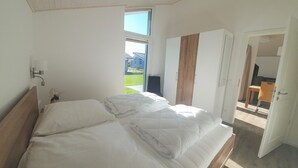 Ein Schlafzimmer mit Bett, Nachttisch, Lampe, Fenster und Blick ins Freie.