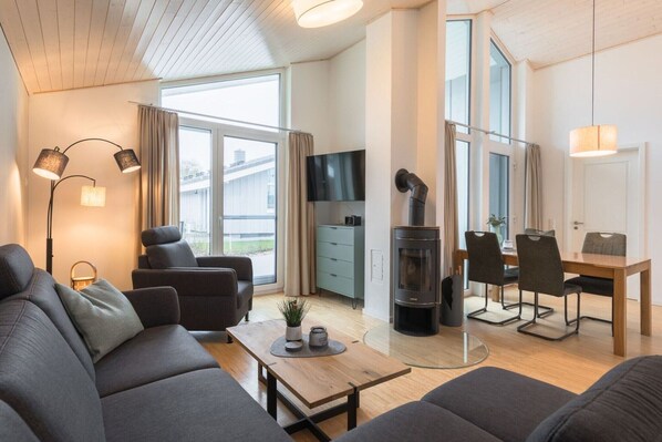 Un salon moderne avec un canapé, une table basse et un téléviseur. On y trouve également une cheminée, un coin repas avec des chaises et, au fond, une cuisine.