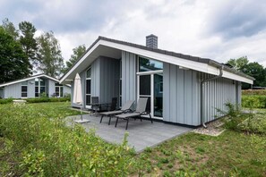 Une maison moderne dotée d’un patio couvert, de grandes fenêtres et d’un jardin bien entretenu.