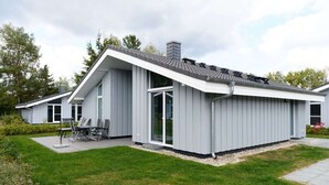 Ein modernes Haus mit geneigtem Dach, großen Fenstern und einer Terrasse mit Gartenmöbeln.