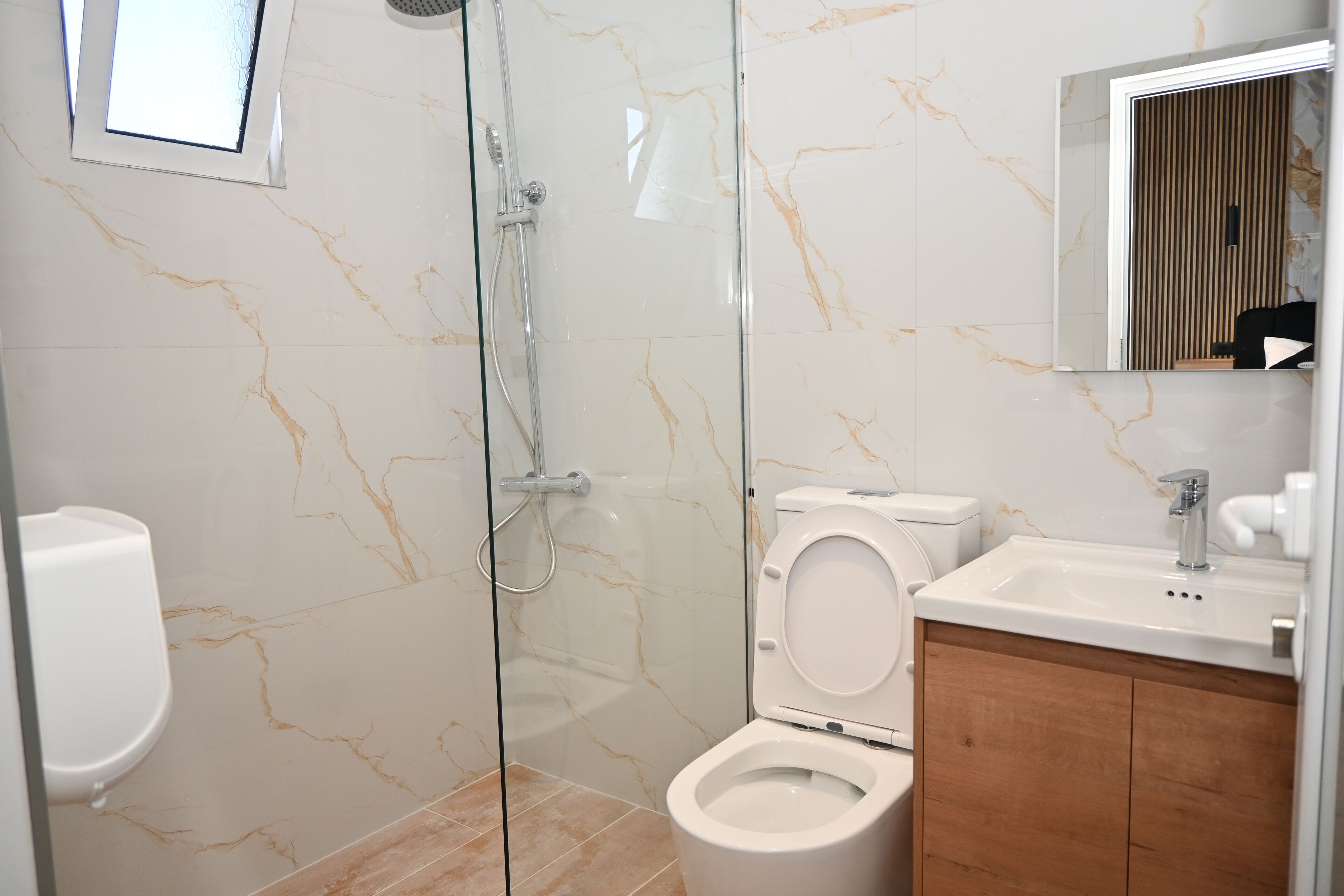 A modern bathroom with a glass-enclosed shower, a toilet, and a sink with a wooden vanity.
