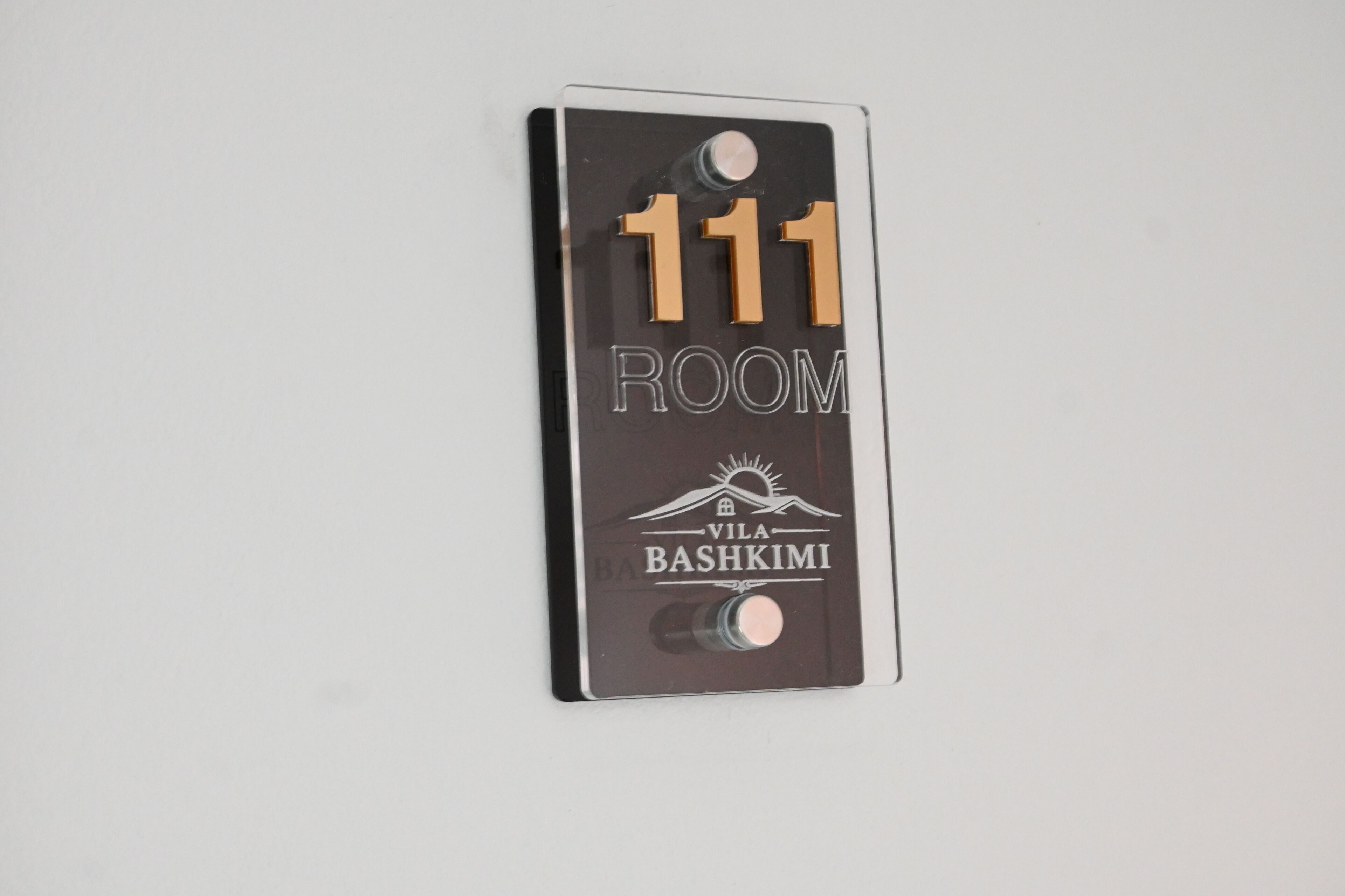 Nummerbord voor kamer 111 bij Vila Bashkimi, met een berg- en zonlogo.
