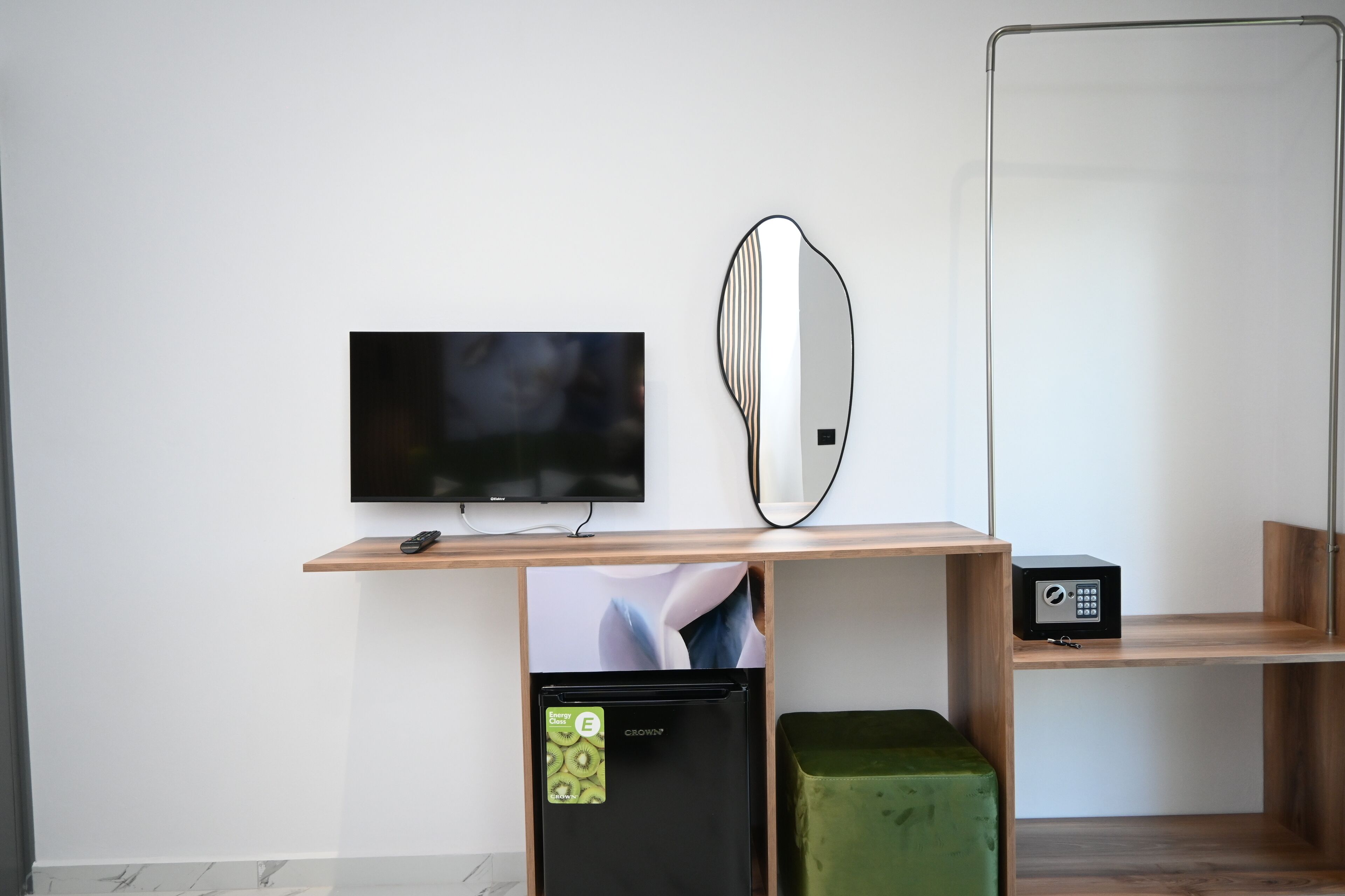 A modern hotel room with a flat-screen TV, a microwave, a green ottoman, and a wooden desk.