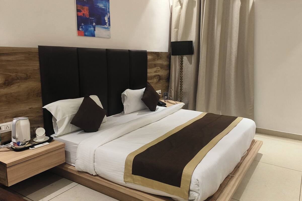 A hotel room with a bed, bedside table, lamp, and a painting on the wall.