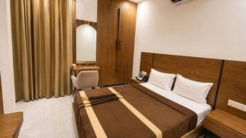 Camera d'albergo con un letto, comodino, scrittoio, sedia, armadio e tende.