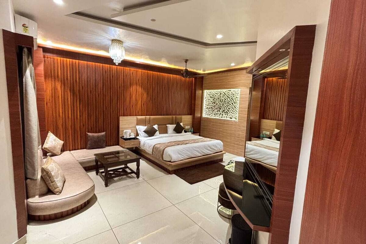 A modern hotel room with a large bed, a sofa, a small table, and a mirror.