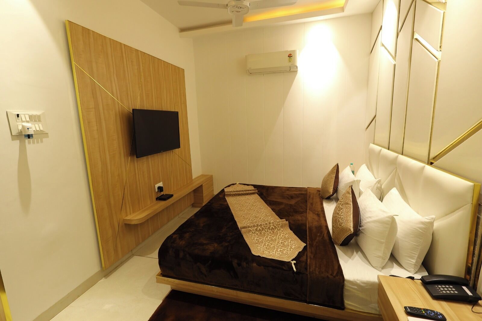Ein modernes Hotelzimmer mit einem Bett, einem Flachbildfernseher an einer Wand aus Holzpaneelen, einem Nachttisch mit Telefon und einer Wand-Klimaanlage.