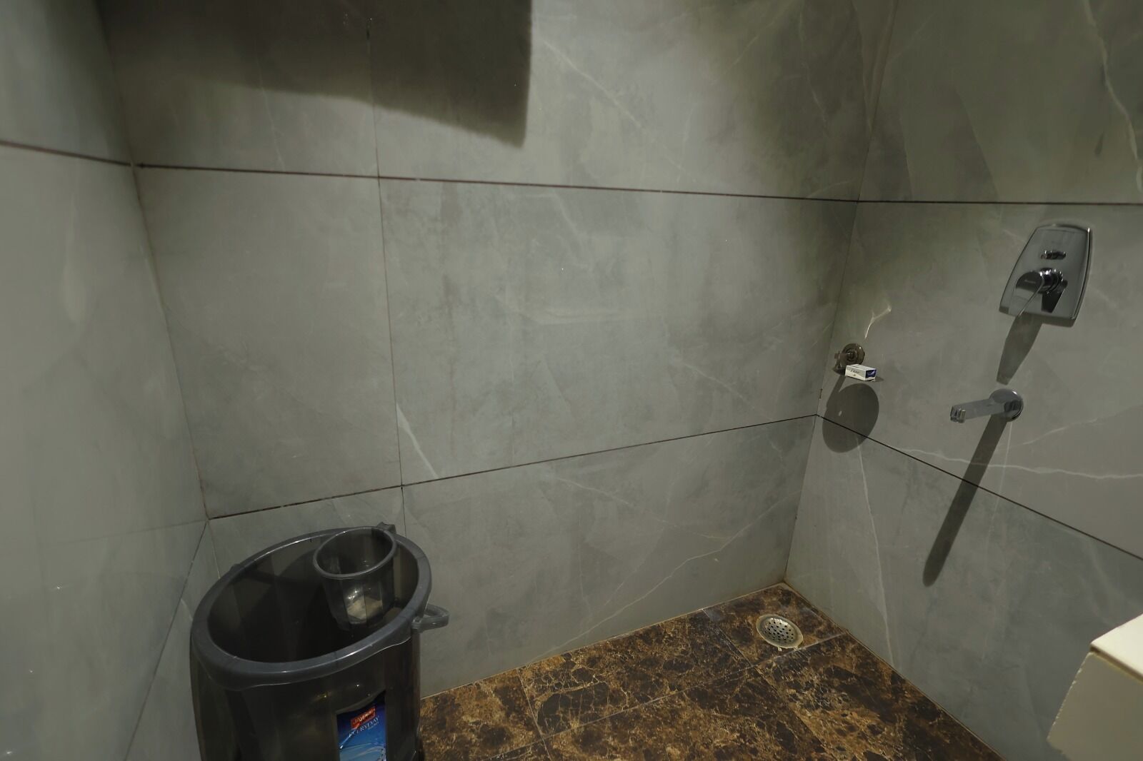 A small bathroom with grey tiled walls, a shower, and a trash bin.